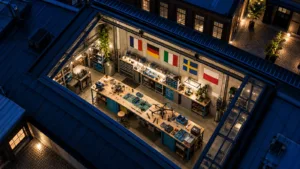 En ung företagare granskar en drönarkonstruktion på en arbetsbänk i en liten svensk teknikverkstad, med en EU-flagga på anslagstavlan i bakgrunden.