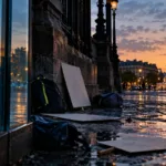 Butiksägare sopar upp glas framför en liten butik med krossat skyltfönster på en gata i Paris efter nattens oroligheter.