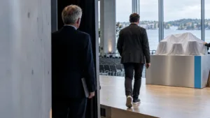 An incoming technology CEO walks toward a product-launch stage while the outgoing leader remains in the background.