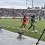 Match de football féminin dans un stade illuminé au crépuscule, avec une tribune de presse partiellement vide au premier plan